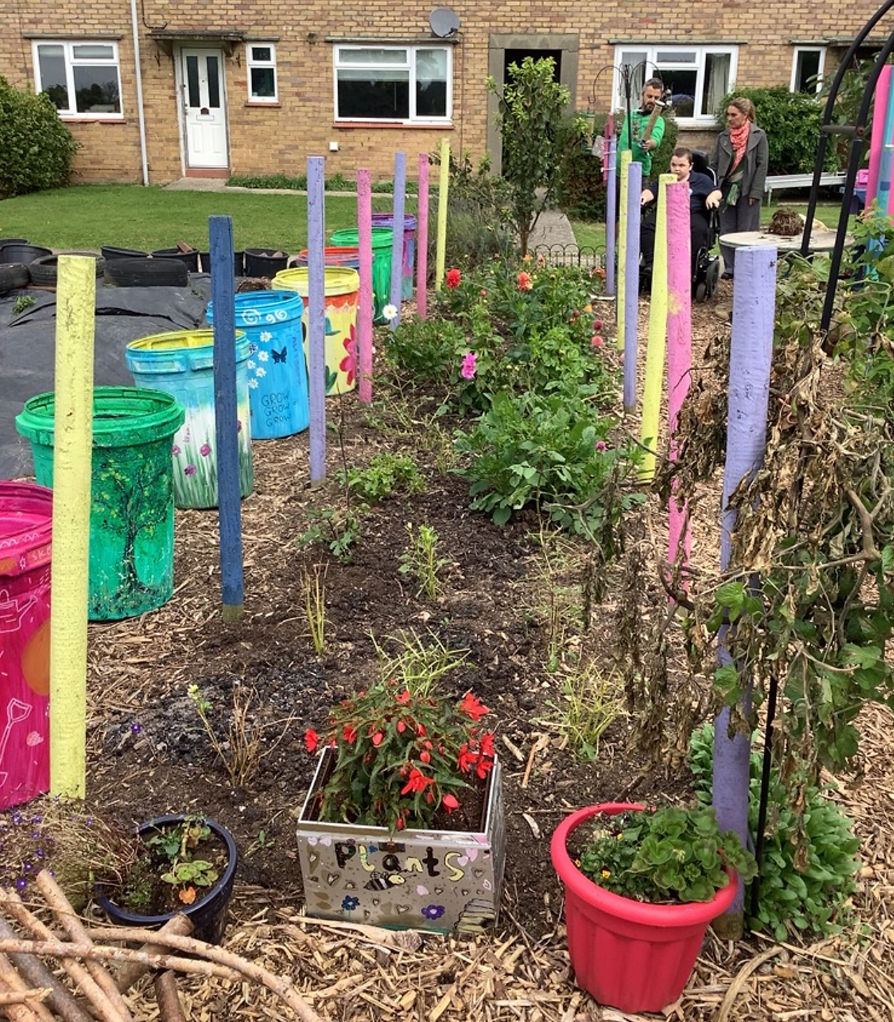 Colorful garden with painted poles and flowers in front of houses.