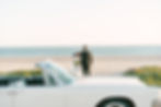 Bride and groom stand on a beach, embracing and smiling. A white convertible is in the foreground, with the ocean and sky in the background. Golden Hour intimate Santa Barbara wedding photography.