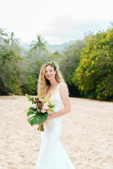 Elegant bride holding a bouquet on a tropical beach, captured in natural light