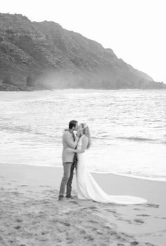 Newlyweds sharing a kiss on the beach in a cinematic black and white photo