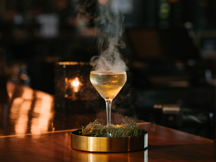 Smoky golden cocktail in dramatic lighting on bar top, photographed for luxury hospitality branding by Anna Kreative Studio.