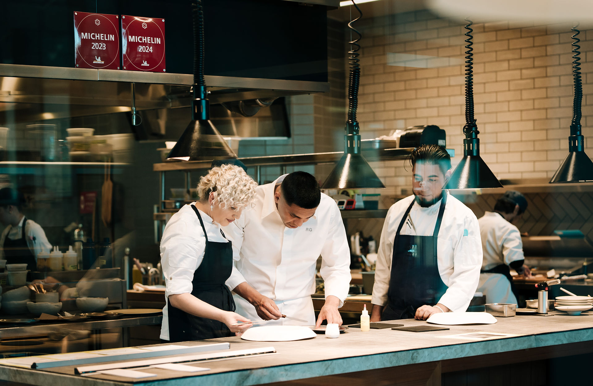 Behind the scenes highlighting the precision and creativity of a world-class restaurant. Group of chefs collaborating in open-concept gourmet kitchen at fine dining restaurant in Montecito captured by the best luxury commercial brand photographer in Santa Barbara and Montecito Anna Kreative Studio