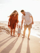 Young family of three photos on the beach in hawaii. A young couple of parents are holding their baby's hand while he is making his first steps on the beach, touching blue ocean waves and smiling. Precious family moments captured in an authentic and genuine way. Unique photography experience for a family of 3 on Oahu. 