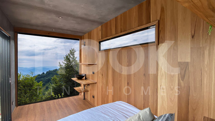 soho modern 20ft studio container home by nook tiny homes with feature concrete and timber wall panels, black tap ware and an open end alfresco behind the cargo doors looking out to a view