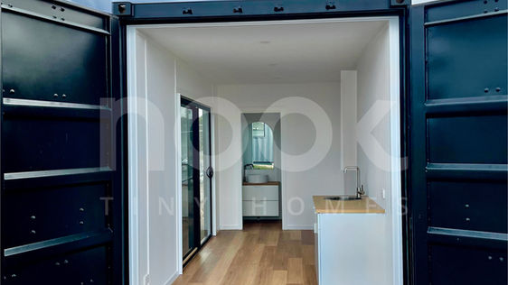 end open view of the palms 20ft studio container home made by nook tiny homes australia, featuring large format sliding window doors, white walls, cabinets, and beautiful timber floors
