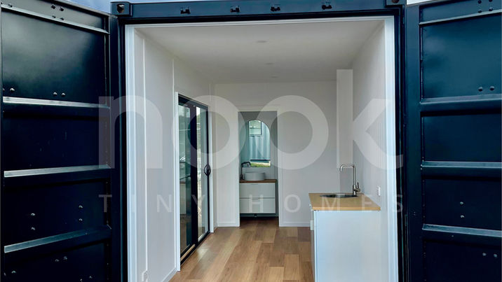 end open view of the palms 20ft studio container home made by nook tiny homes australia, featuring large format sliding window doors, white walls, cabinets, and beautiful timber floors