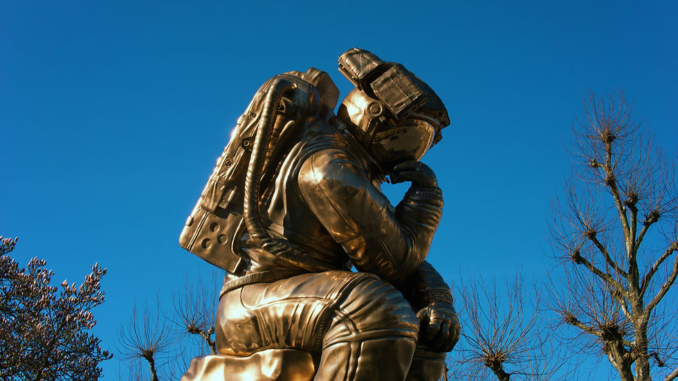 Bronze astronaut statue kneels under a clear blue sky, framed by bare winter trees.