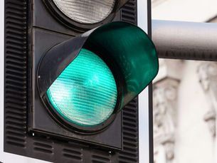Close-up of a glowing green traffic light against a blurred city building background.