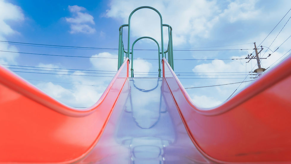 Low-angle view up a glossy red-and-purple playground slide under a bright blue sky with clouds and power lines.