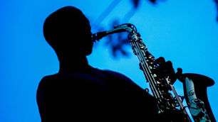 Silhouette of a saxophonist playing on a blue-lit stage, creating a moody, dramatic scene.