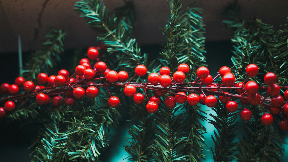 Close-up of glossy red berries on evergreen branches, creating a festive holiday wreath-like texture against a dark background