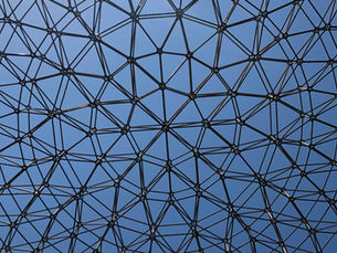 Black geometric lattice dome against a blue sky, forming a web-like canopy overhead.