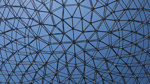 Black geometric lattice dome against a blue sky, forming a web-like canopy overhead.