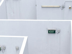 White stairwell wall with three green EXIT signs, a fluorescent light and alarm fixtures, bright geometric shadows.