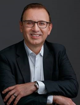 Santos Vera wearing glasses and a suit, posing for a portrait photo.