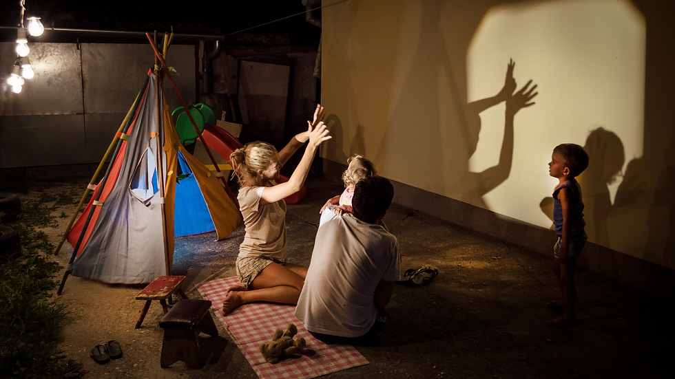 Family creates shadow puppets on a wall by a tent at night, illuminated by warm light. Two children watch, creating a playful mood. Focus on storytelling to build a Strong Brand Identity for Your Startup.
