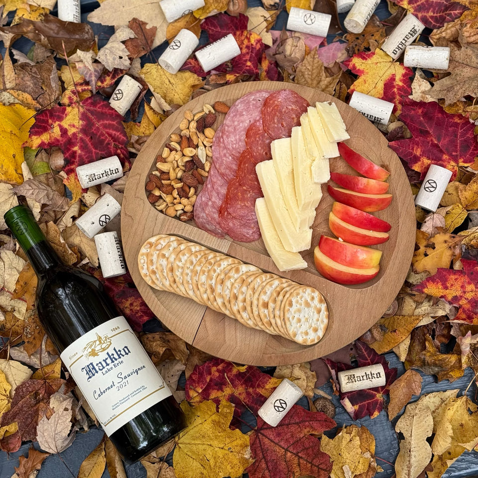 Image of Markko Cabernet Sauvignon in the fall leaves next to a charcuterie board of meat, fruit, and crackers