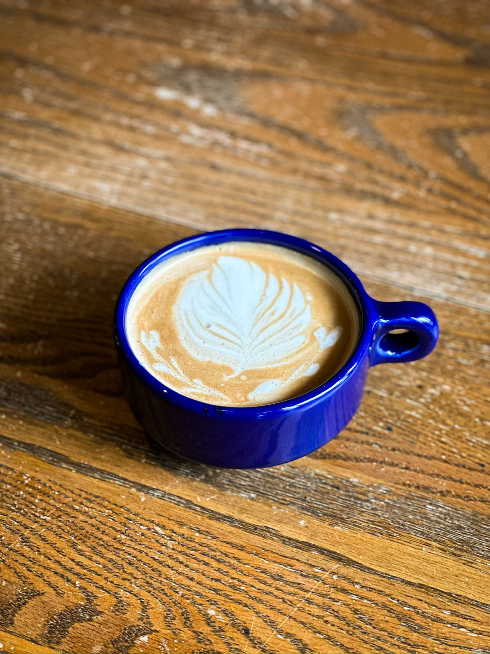 Image of a latte with latte art in the shape of a leaf in a blue cup on a wooden table