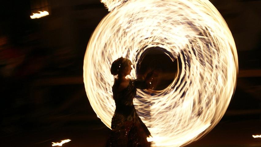 Frau als Silhouette, dreht Feuerseile so, daß sie wie eine brennende Scheibe aussehen