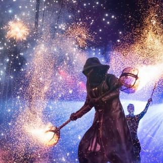 Ein mystischer Darsteller in einem schwarzen Mantel führt eine beeindruckende Feuershow auf, umgeben von funkelnden Funken und Lichtern. Perfekt für spektakuläre Shows, Märchen-Events und Dinner-Inszenierungen.