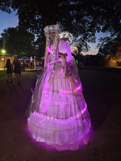 Eine beeindruckende Lichterfee in einem leuchtenden Kostüm mit funkelnden Lichtern, die bei Nacht durch einen Park schreitet. Perfekt für märchenhafte Walk Acts, Shows und besondere Dinner-Events.