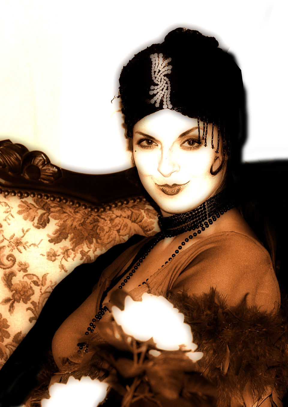 20er Flapper Diva historischer Walk Act, Sepia Vintage Portrait Filmdiva Zwanziger Jahre mit Schmuck Turban über dunkle zwanziger Jahre Bobfrisur, lange schwarze Perlenketten, sitzt auf antikem Sofa und lächelt mit Kußmund