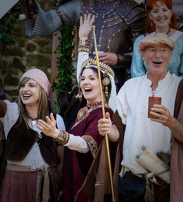 Roswitha (Hrotsvit) von Gandersheim, Theater und historischer Walk Act, erste bekannte deutsche Dichterin aus dem 10. Jhdt., Theater, Gedicht, Vortrag, Lesung und Walk Act in früh mittelalterlichem Gewand, byzantinische Mode in roter Seide mit Stickereien, aufwendigem Hals- und und Schapel Kopfschmuck byzantinische Mode in rot und gold, hebt die Hand und jubelt strahlend mit anderen Darstellern, "Gesta Oddonis" über die Taten Otto I des Großen. bei Veranstaltungsreihe "Des Kaisers letzte Reise"