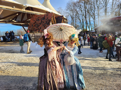 Zwei Darstellerinnen in aufwendigen Rokoko-Kostümen und mit einem Sonnenschirm spielen die Stiefschwestern aus einem Märchen auf einem winterlichen Event. Perfekt für Märchen-Walk Acts und Shows.