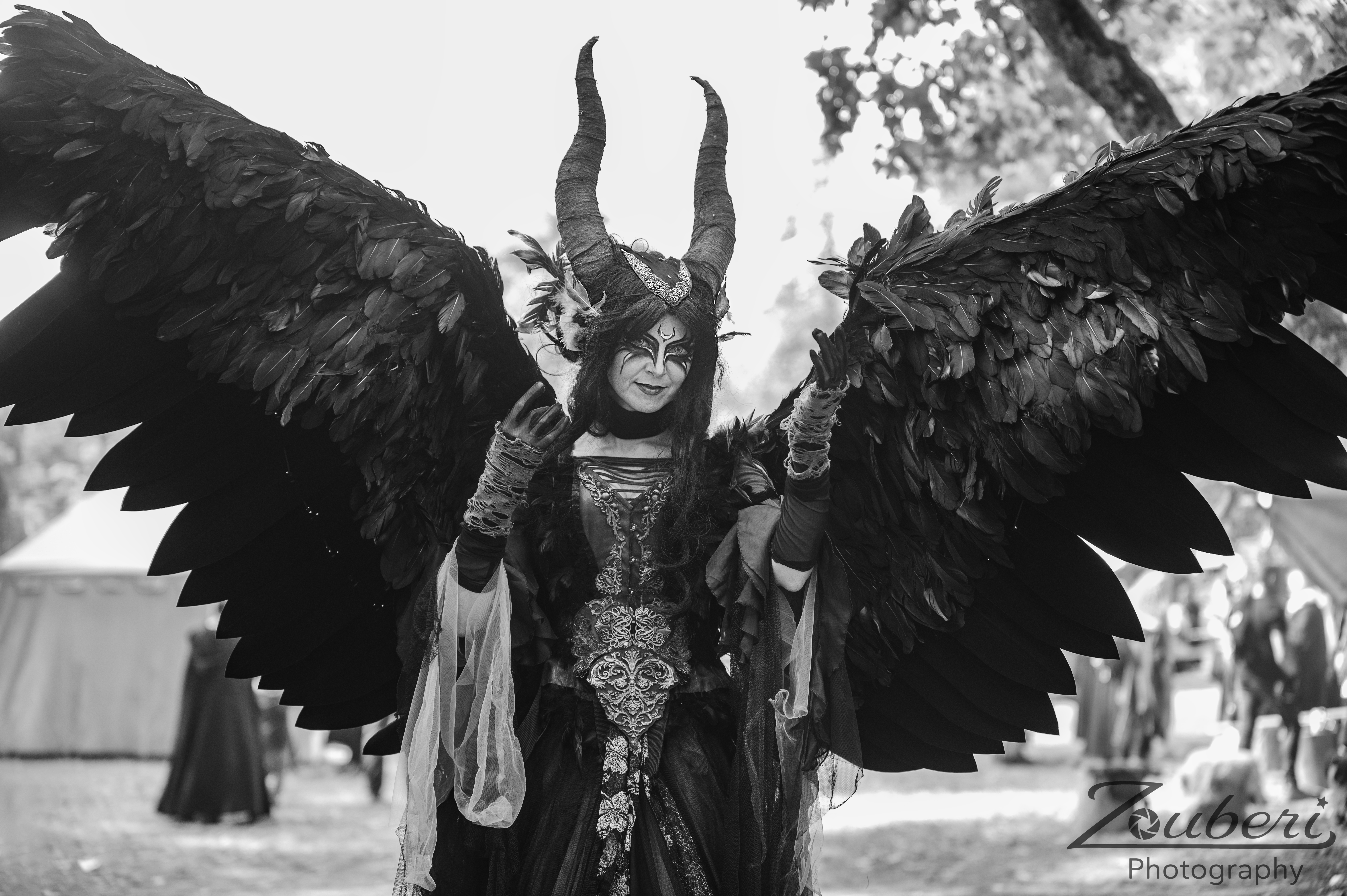 Stelzenläuferin in einem detailreichen Dämonen-Kostüm mit großen schwarzen Flügeln, Hörnern und aufwendigem Make-up, bei einem Walk-Act auf einem Mittelalter- Fantasy-Festival