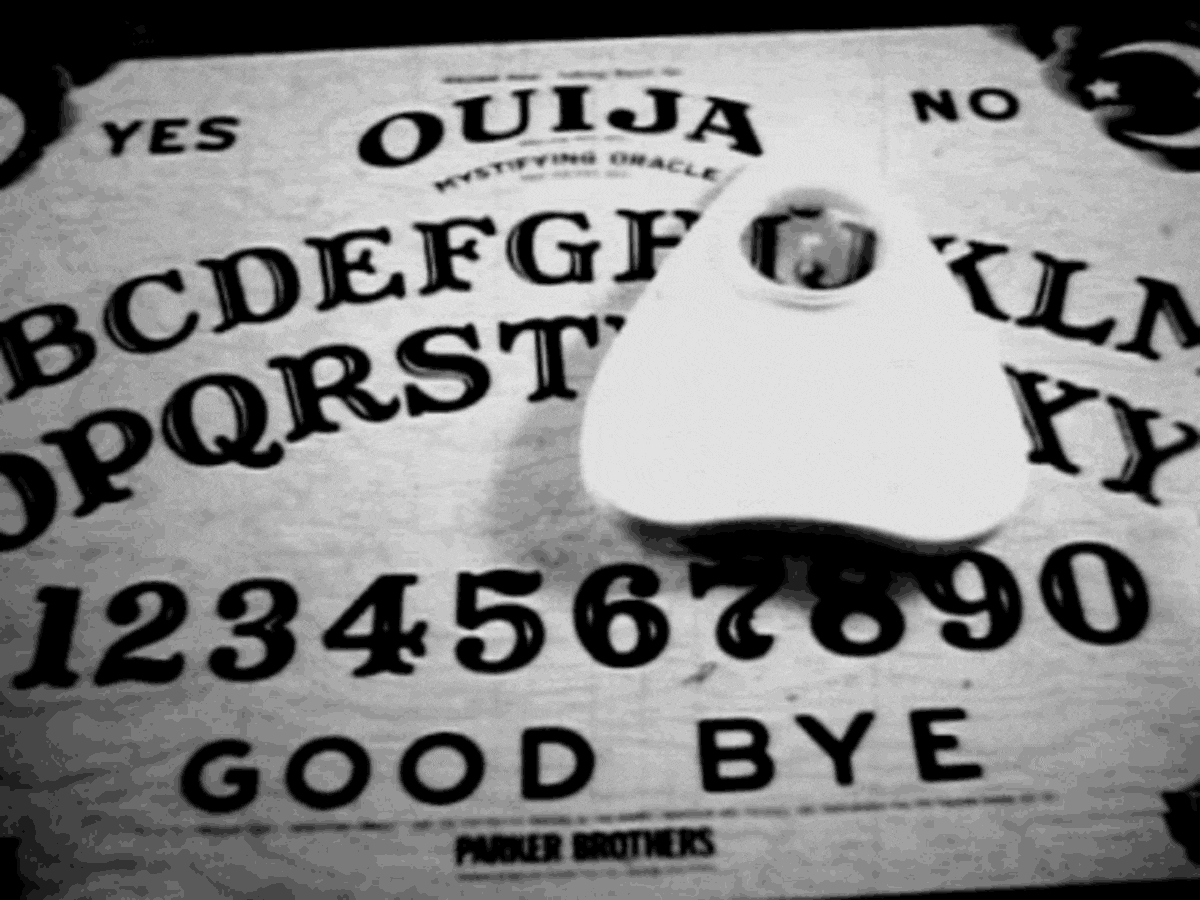 Ouija board with planchette, letters, numbers, and words "YES," "NO," "GOOD BYE." Mystical atmosphere, black and white image.