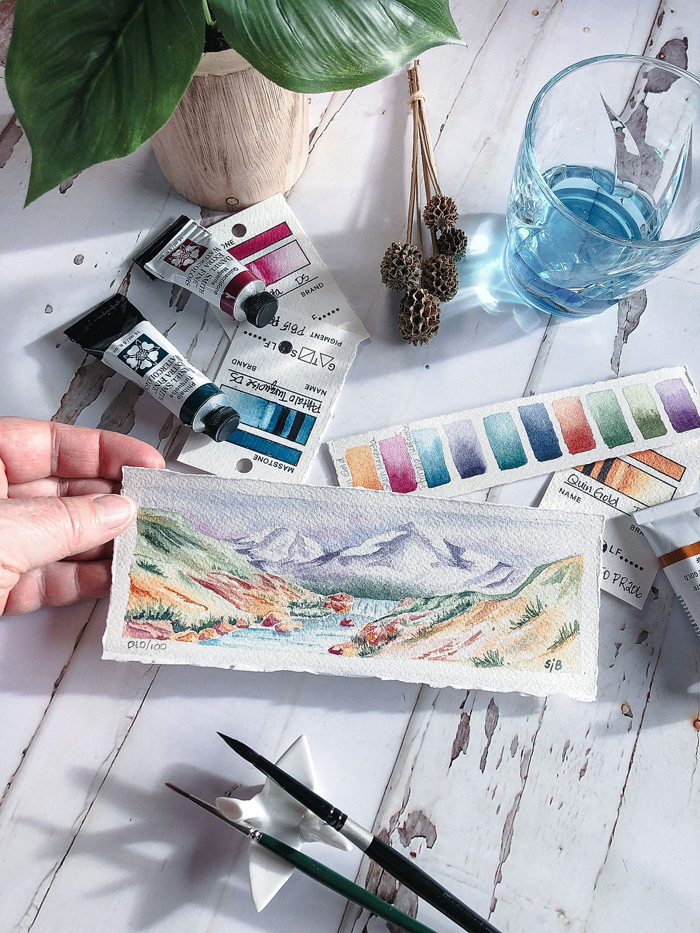 Thumbnail: watercolor landscape of mountain stream and waterfall flowing from mountain range, colorful, artist holding