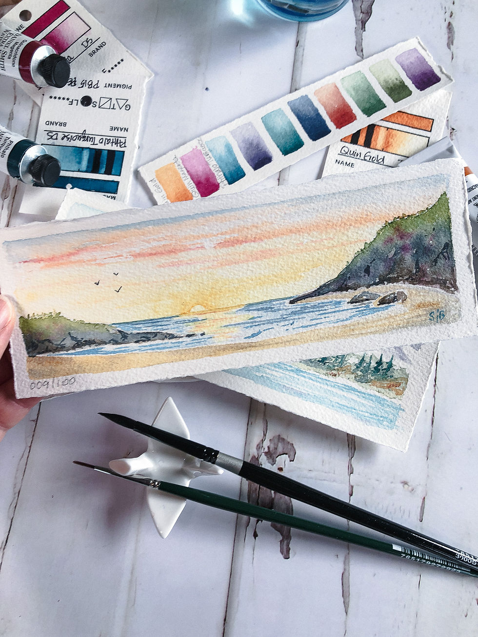 Thumbnail: watercolor landscape of ocean sunset, yellow and orange sky, artist holding