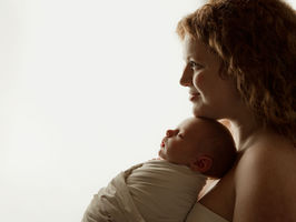Newborn baby girl peacefully sleeping in a white wrap and bow, posed on a soft neutral blanket in a professional Aurora Colorado newborn photography studio with natural light.