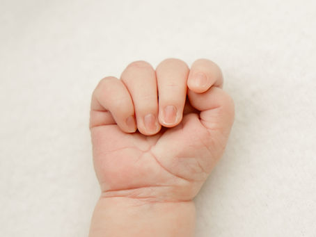 Close-up of a newborn baby’s hand resting gently on a soft neutral background.