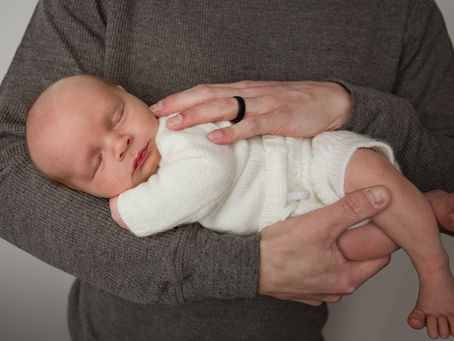 Father holding a sleeping newborn baby safely in his arms during a professional newborn photography session in Aurora, Colorado.