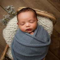 Newborn baby Eliab wrapped in blue fabric and posed in a basket with natural textures in Aurora newborn photography studio