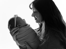 Black and white portrait of a mother holding her newborn baby close, gazing at her infant wrapped snugly, capturing a quiet, emotional moment of connection.