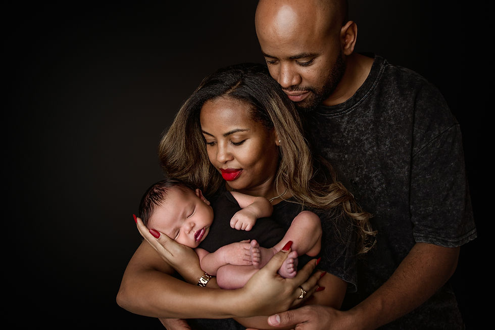 Parents holding newborn baby Eliab in a soft, intimate portrait with dark background lighting in Aurora newborn photography studio