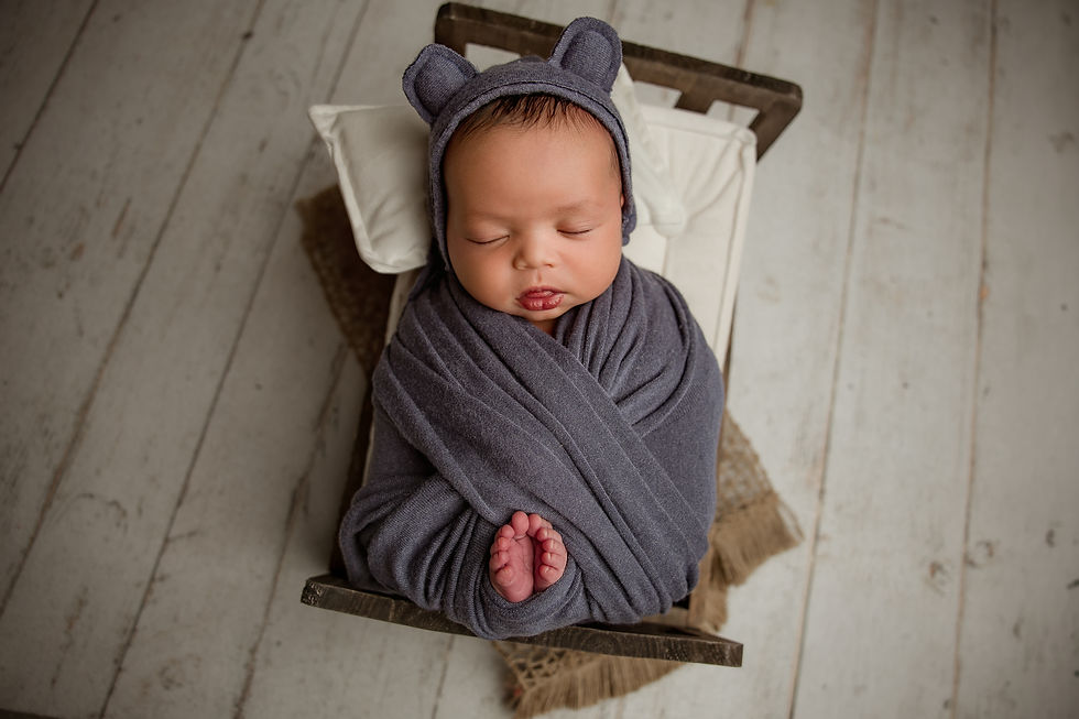 Newborn baby Eliab wrapped in gray fabric with a knit bonnet, posed in a wooden prop during Aurora newborn photography session