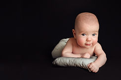 Sweet image of  new baby boy laying on belly making a sweet smile face wile looking dead into the camera on a black background