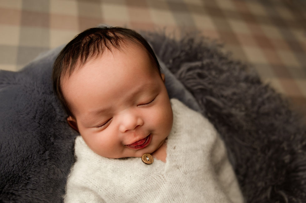 Newborn baby Eliab smiling while resting on a soft textured blanket during an Aurora newborn photography session