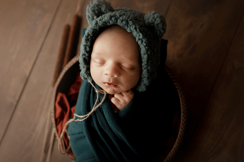 Aurora Colorado | Newborn Photographer | Tiny Details Photography | New baby girl wrapped in criss cross green wrap on matching green bunny fur and fabric background wrapped with toes out and wearing a crocheted green bonnet while smiling