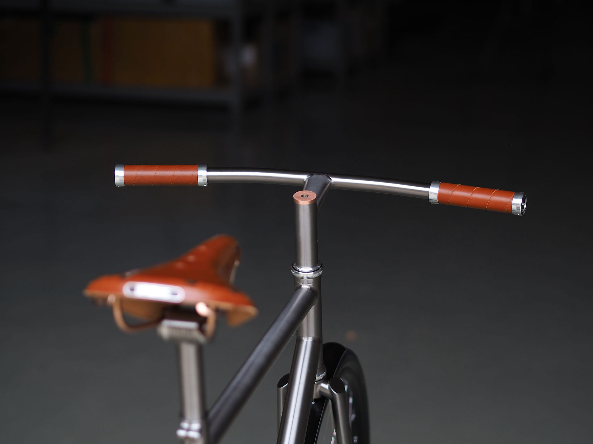 Close-up of the Nua Classica custom titanium cockpit, showing the seamless stem and handlebar integration, unicrown fork, and Brooks leather grips with copper details.