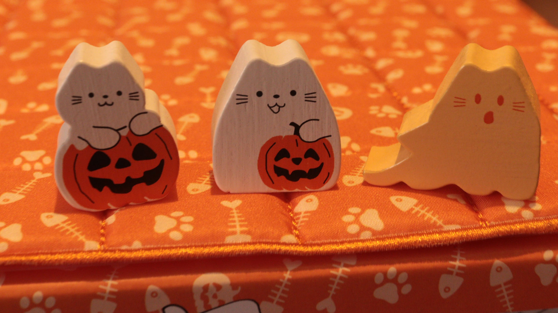 Meeples from left to right on top of the game quilt from BOOoop. the white pumpkin Kitten, white pumpkin Cat and orange Ghost Cat