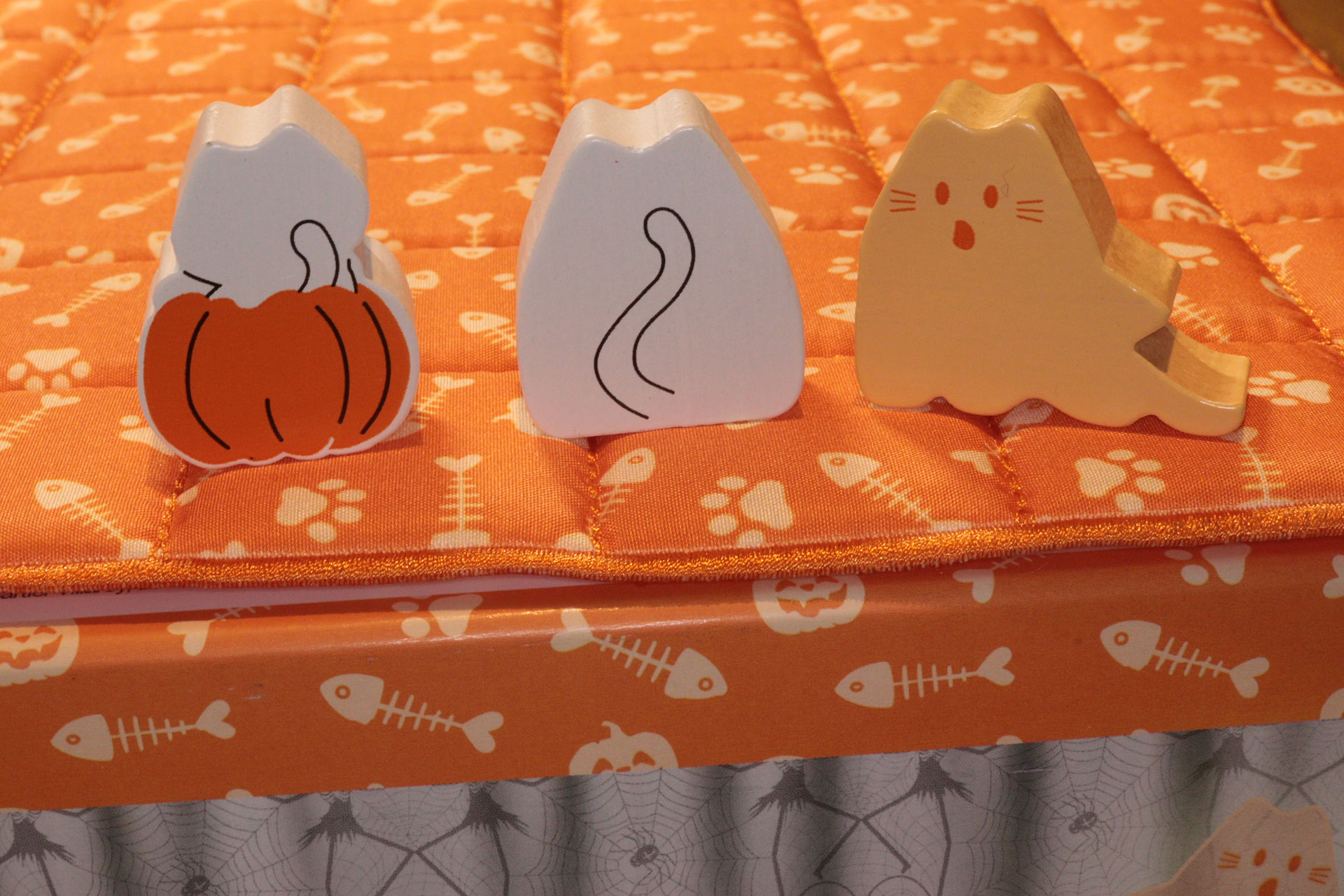 The reverse side of meeples from left to right on top of the game quilt from BOOoop. the white pumpkin Kitten, white pumpkin Cat and orange Ghost Cat