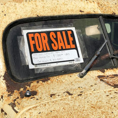 Old rusty car parked with a hand-written 'For Sale' sign in the window