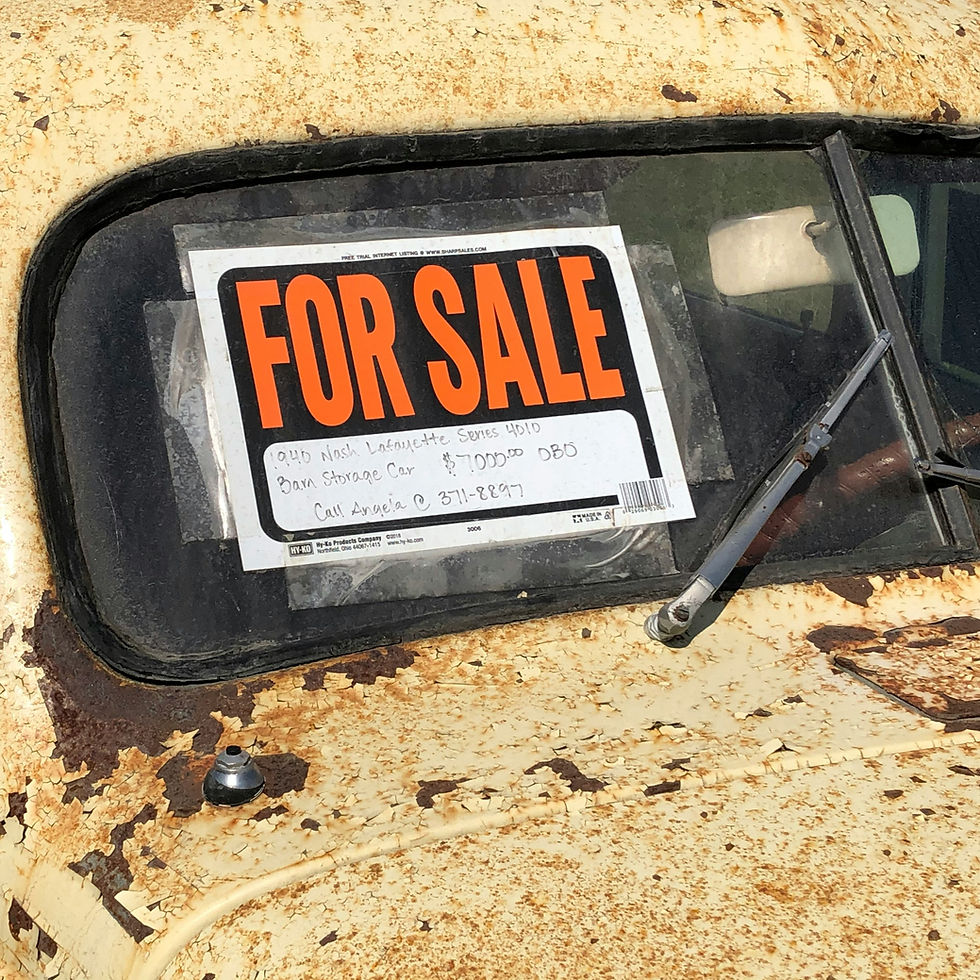 Old rusty car parked with a hand-written 'For Sale' sign in the window