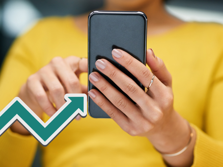 Person in a yellow sweater uses a smartphone, focus on hands. Green upward arrow symbol suggests progress or growth.
