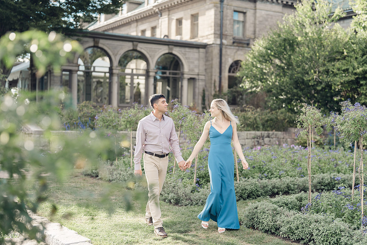 Adam and Bekah walk the formal gardens at Eolia Mansion at Harkness Park, hand-in-hand smiling with the mansion behind them