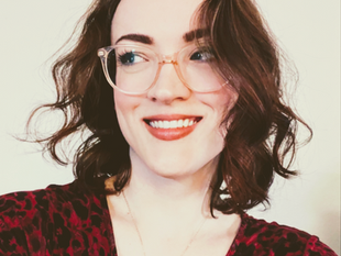 Photo of woman with short dark hair and clear glasses smiling and looking away from camera